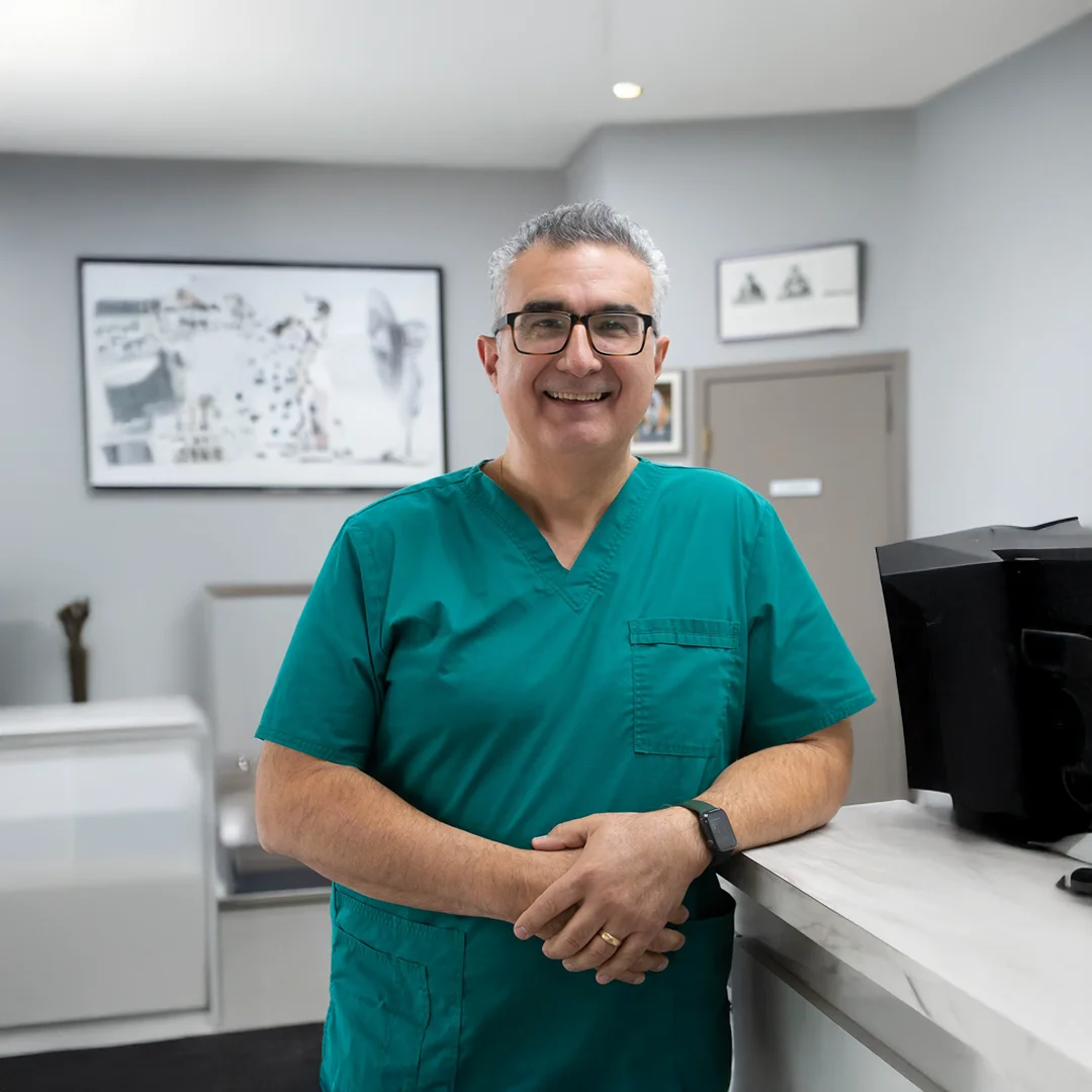 Dr. Carlos Abdul-Chani smiles while standing in a teal scrub top inside Byram Animal Hospital with pet-themed artwork on the wall behind him.
